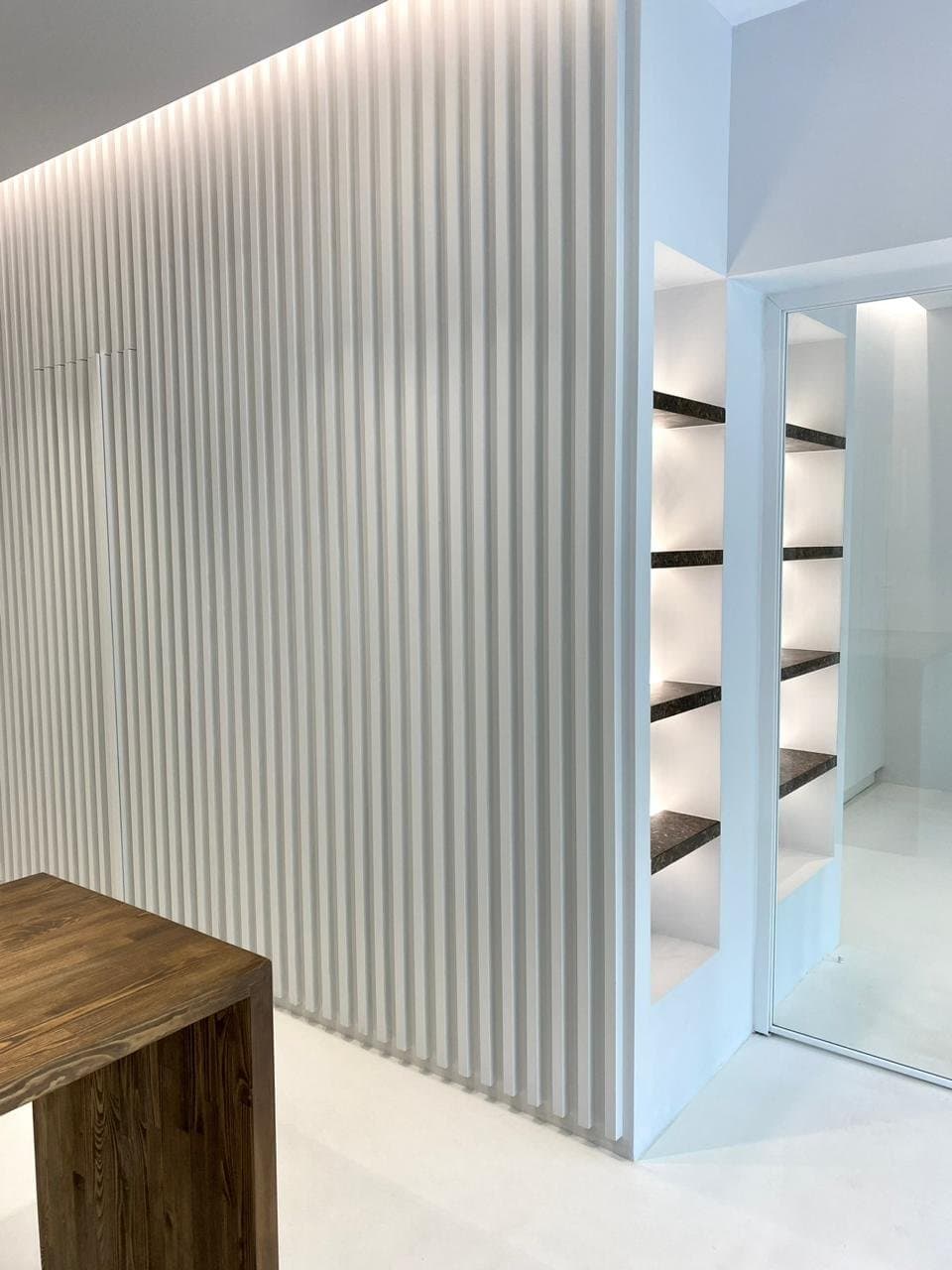 Floating PHEE Board shelves in a backlit niche, beside the ribbed white wall