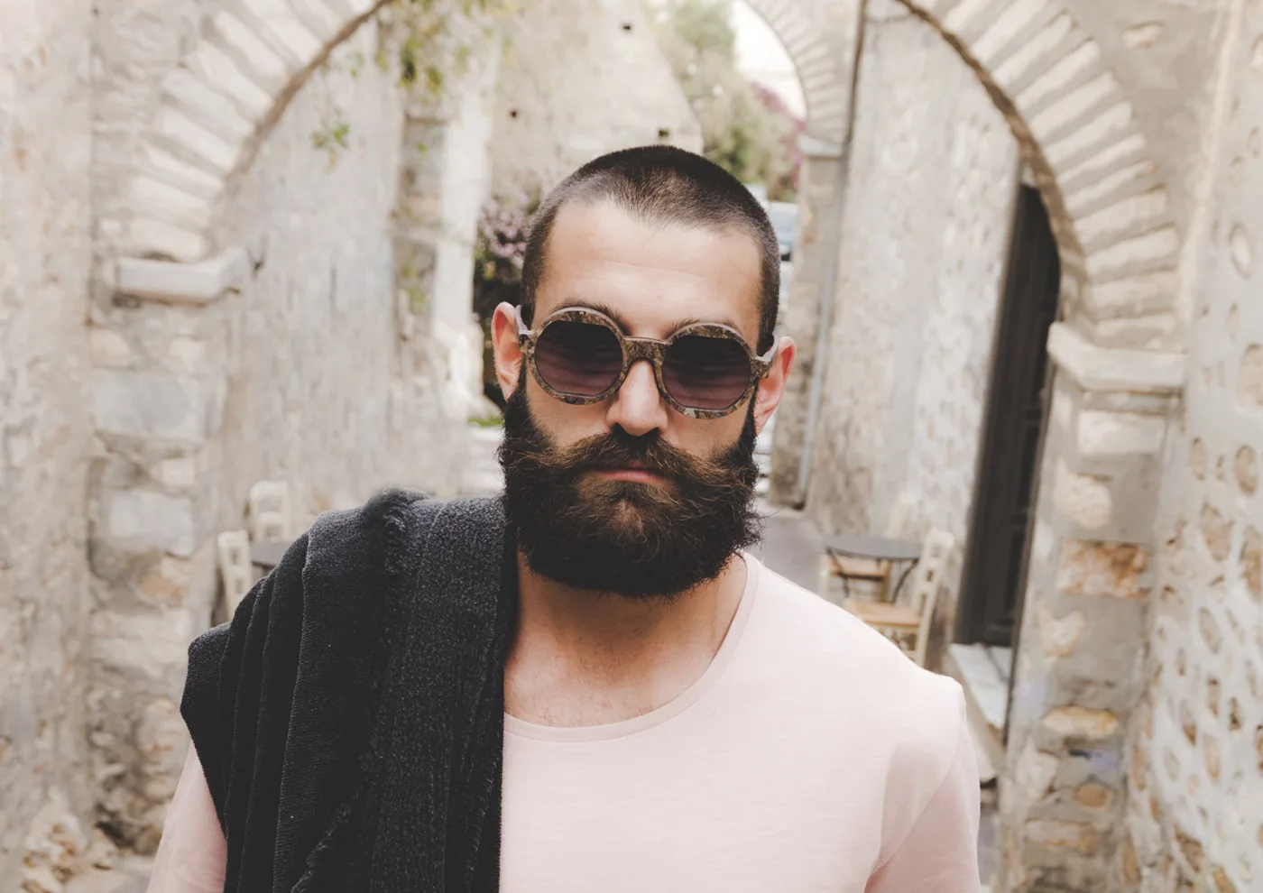 A man wearing round Zeyelo seagrass sunglasses in a stone alley on Syros