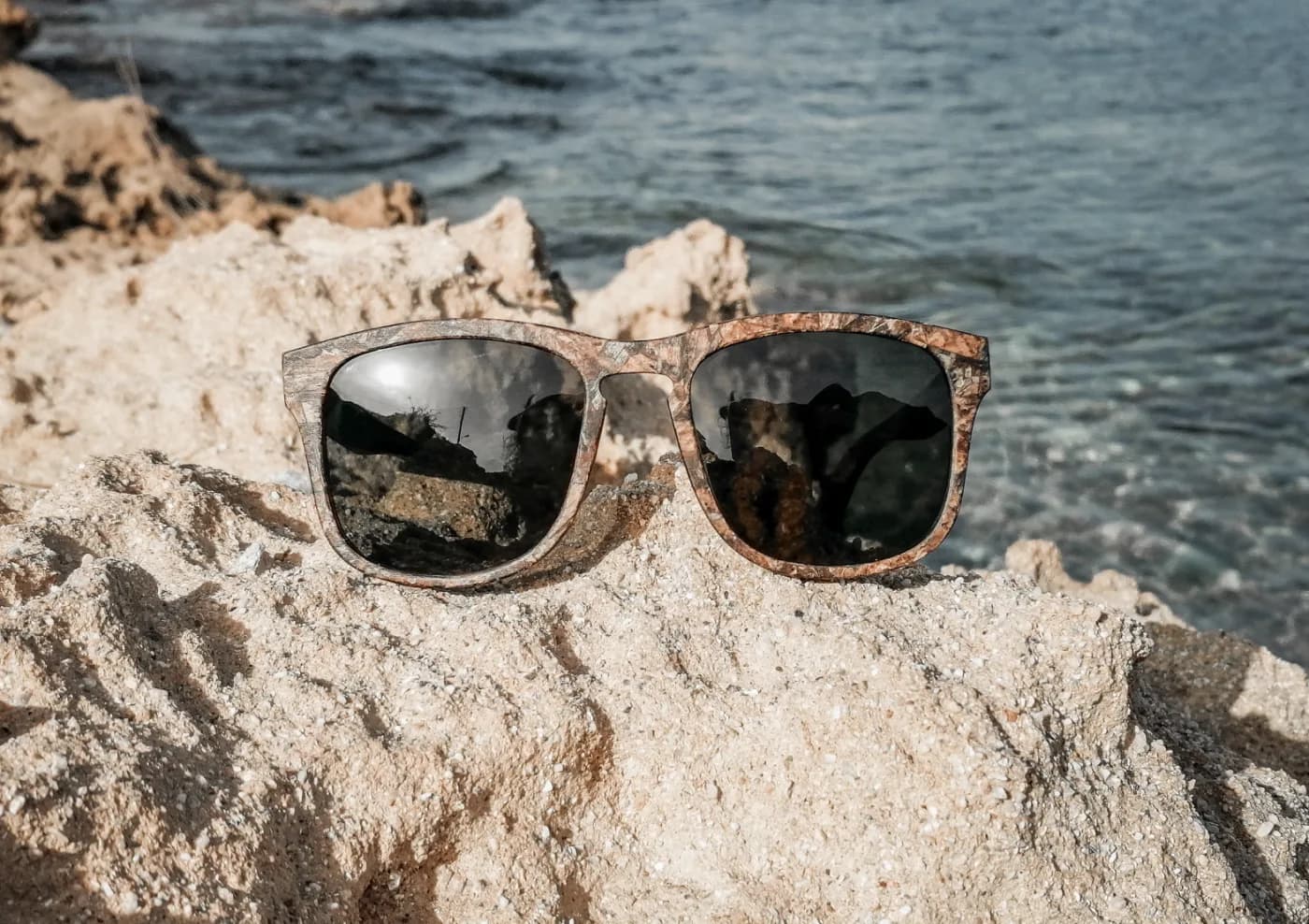 Zeyelo wayfarer sunglasses in natural seagrass on a sunlit coastal rock